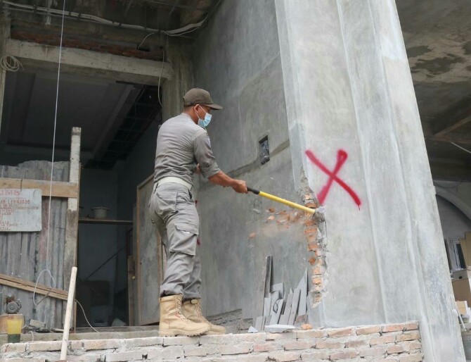 Salah seorang personel Satpol PP Kota Medan sedang menghancurkan dinding bangunan rumah mewah yang menyalahi izin di Jalan Katelia Kecamatan Medan Helvetia, Selasa (22/2/2022). Foto:ist