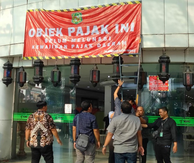 Tim Bapenda Kota Medan dan Personel Satpol PP Kota Medan sedang memasang spanduk penunggak pajak di Gedung Yuki Simpang Raya Medan, Sabtu (12/5/2023)