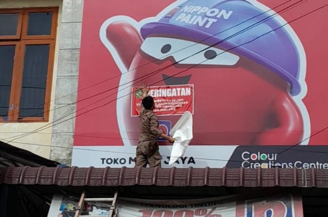 Personel Satpol PP Kota Medan menempelkan stiker tanda tidak bayar pajak di salah satu reklame merek toko di Kota Medan