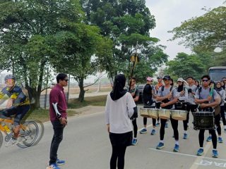 DRUM BAND: Seorang pesepeda melintas di hadapan formasi tim Drum Band Sumut yang tengah menjalani latihan di kawasan Jalan Arteri Kualanamu, Sabtu (3/8/2024). Drum band Sumut semakin matang dalam taktik dan fisik untuk meraih 7 medali emas di PON 2024.(HO/kaldera)